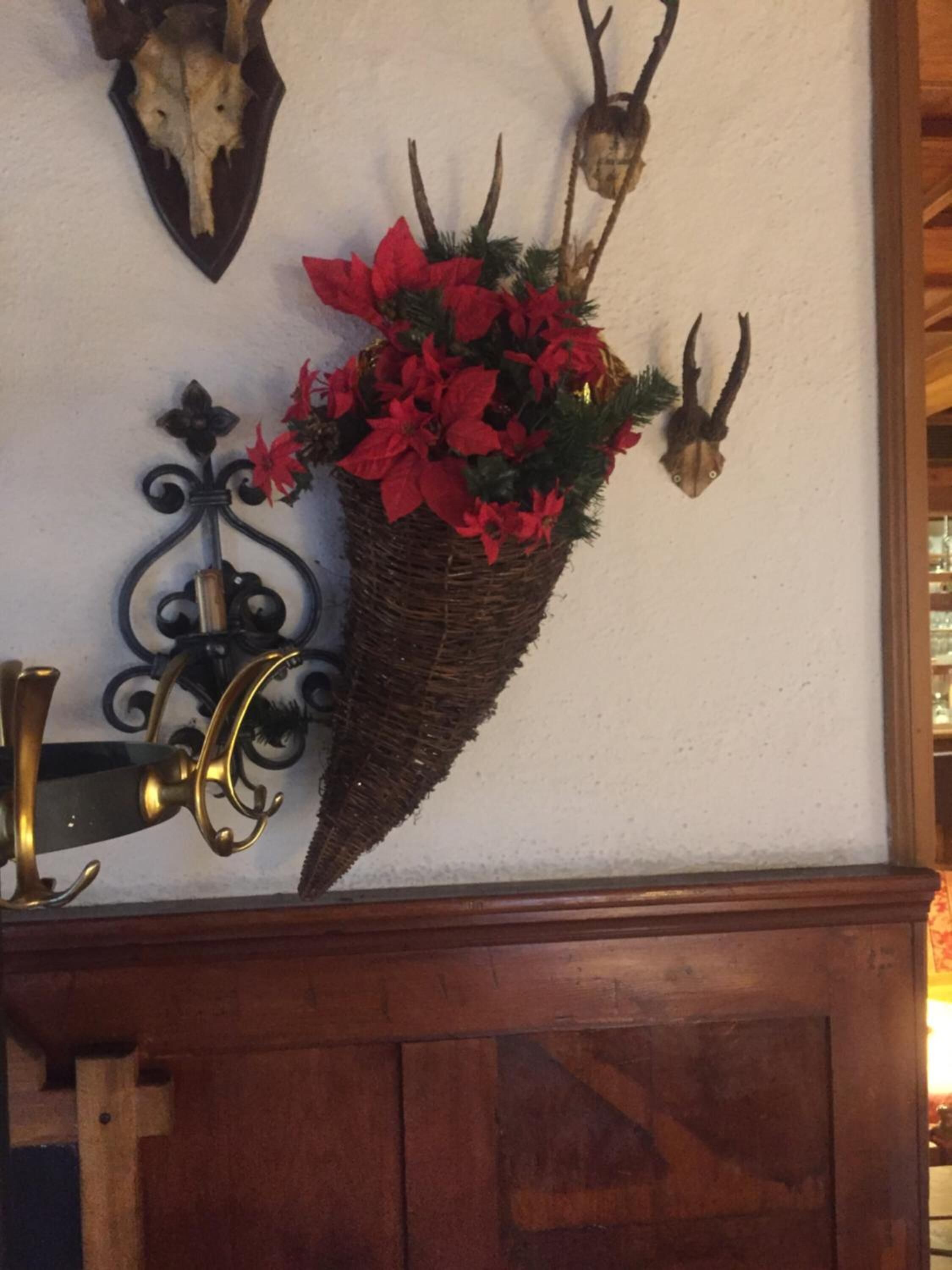 Un adorno de pared con un cesto de flores de poinsettia rojas, una calavera montada y una cabeza de ciervo montada.