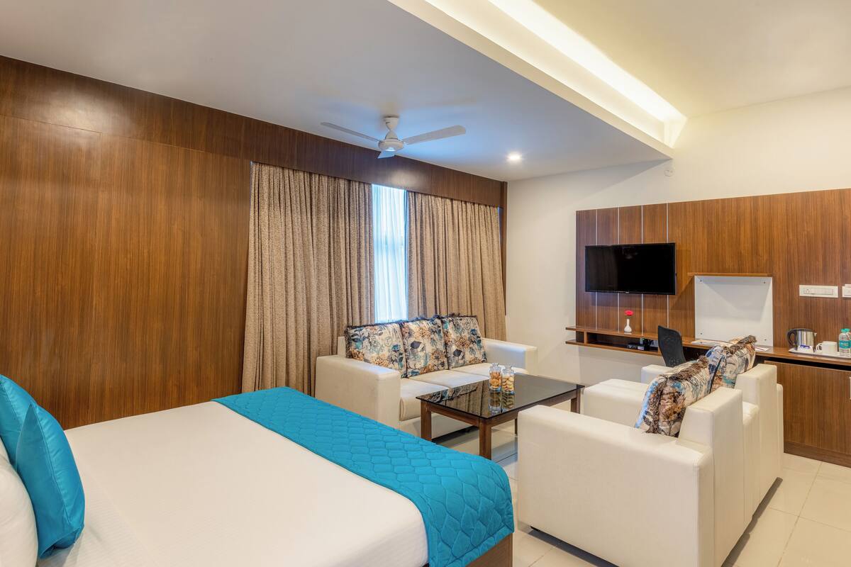 A hotel room with a bed, a sofa, a coffee table, a desk with a TV, and a ceiling fan.