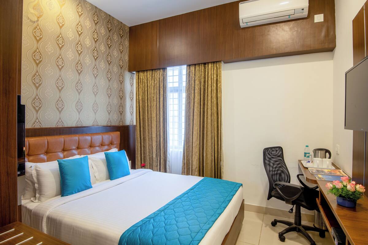 A hotel room with a large bed, a desk with a computer, a chair, and a TV.