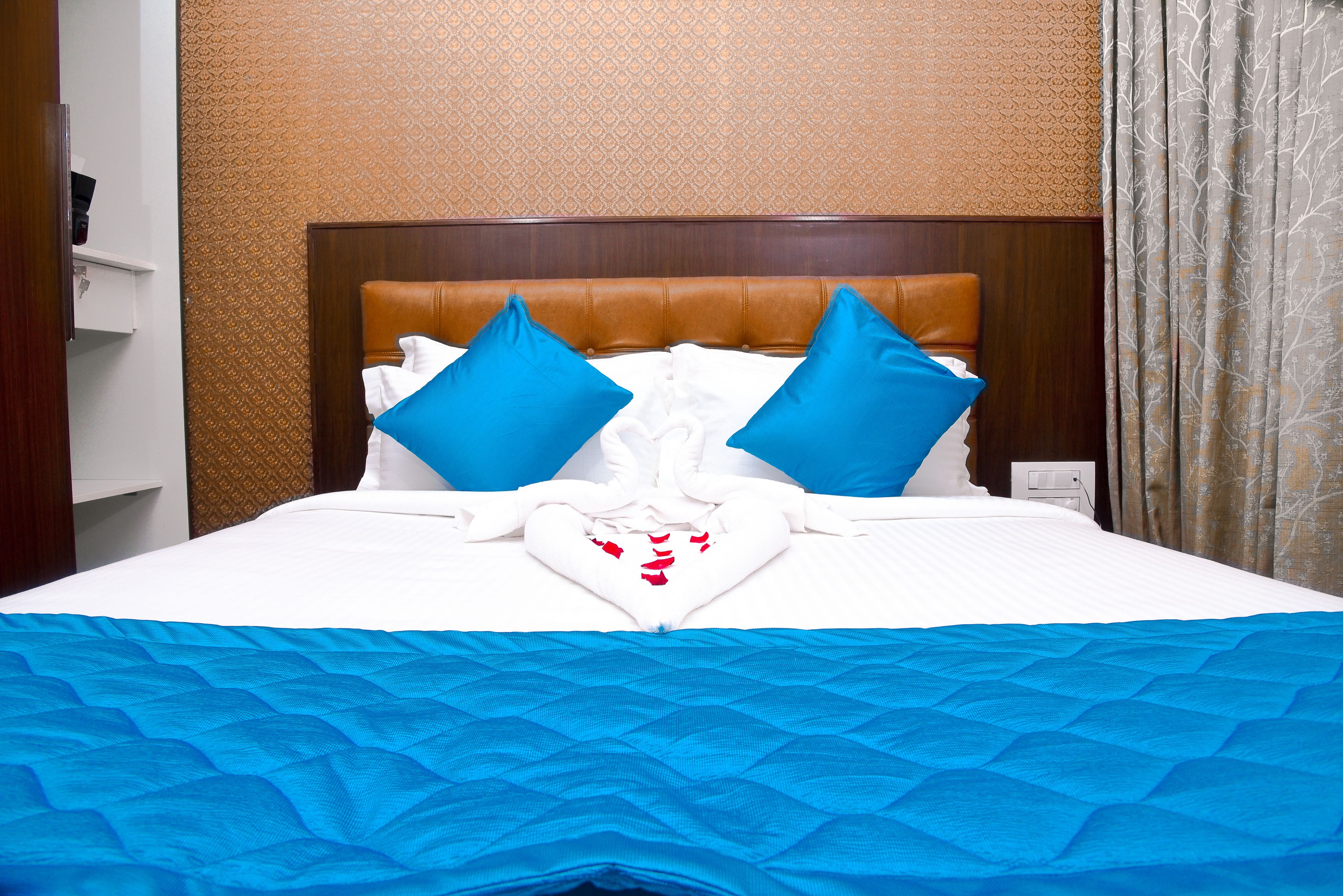 A hotel room with a large bed, two blue pillows, a white comforter, and a blue bedspread.