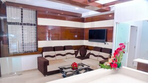 A modern living room with a sectional sofa, a glass coffee table, and a flat-screen TV mounted on the wall. - Hotel Blue Ocean Residency (Bengaluru)