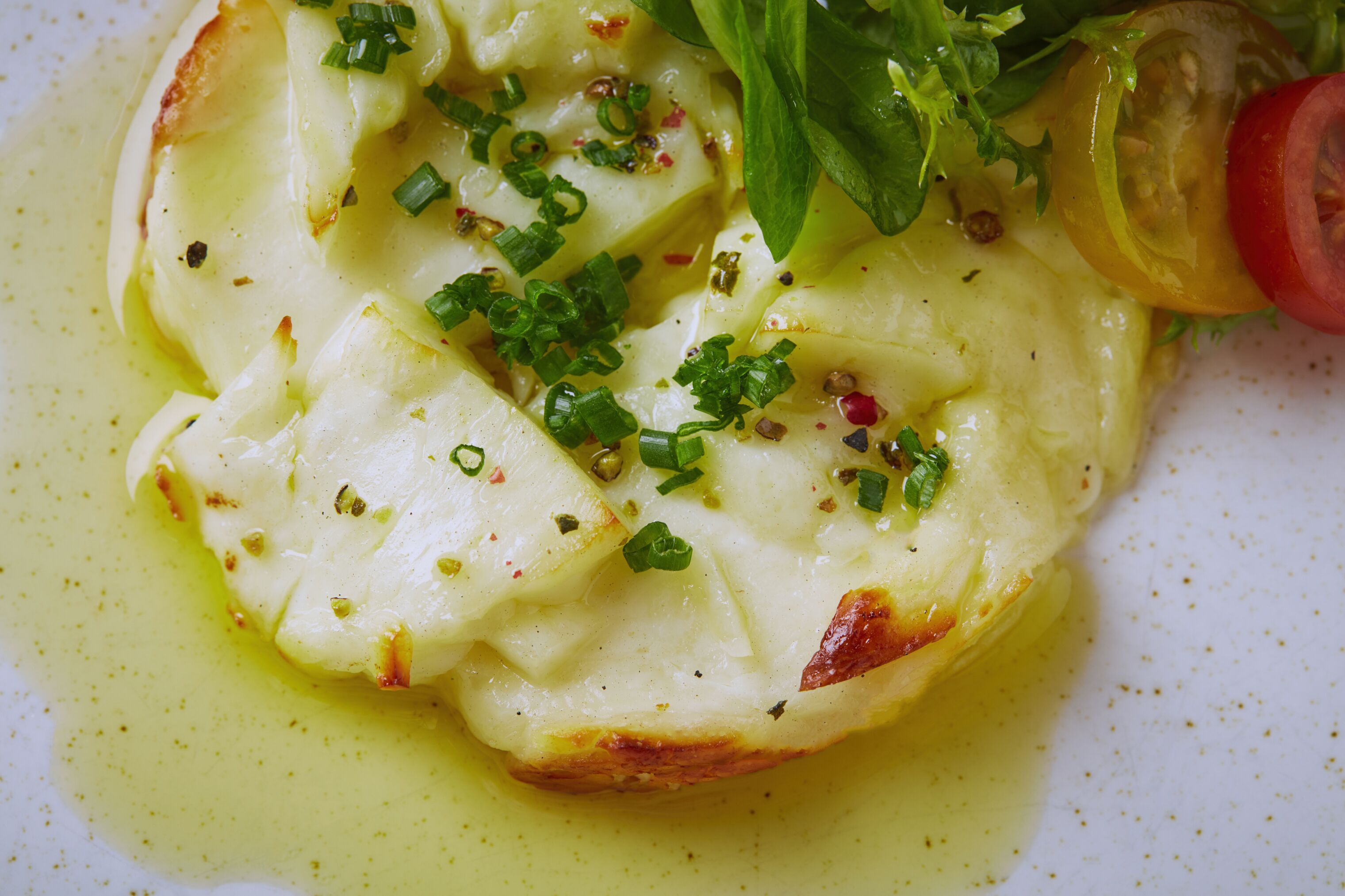 Close-up de um prato com molho cremoso, cebolinha verde e uma fatia de tomate em um prato branco.