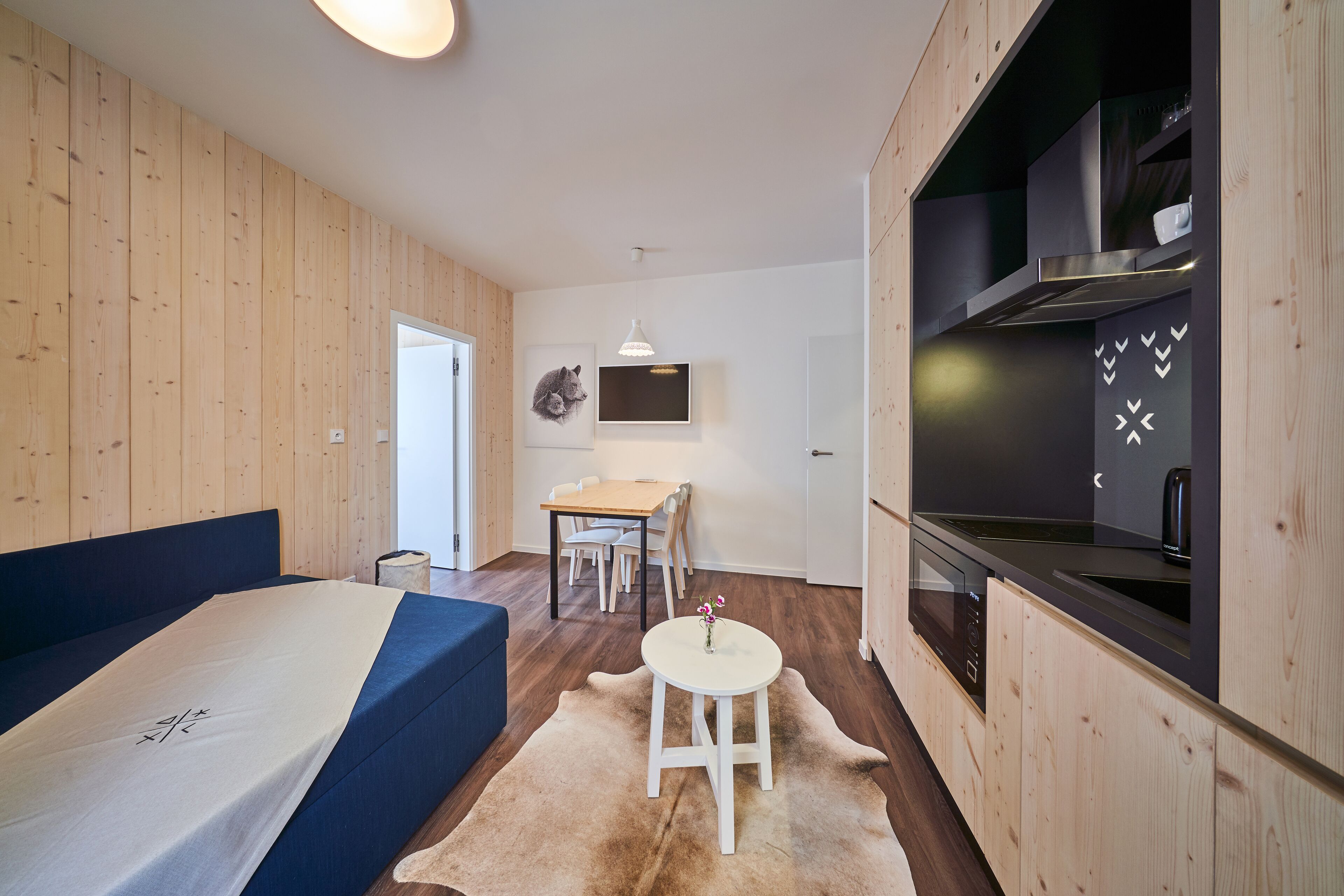 A modern room with a bed, a dining table, and a kitchen area.