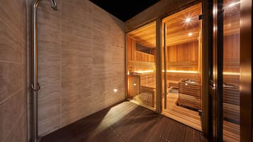 A modern sauna with wooden walls and a glass door, a metal handrail, and a wooden deck.