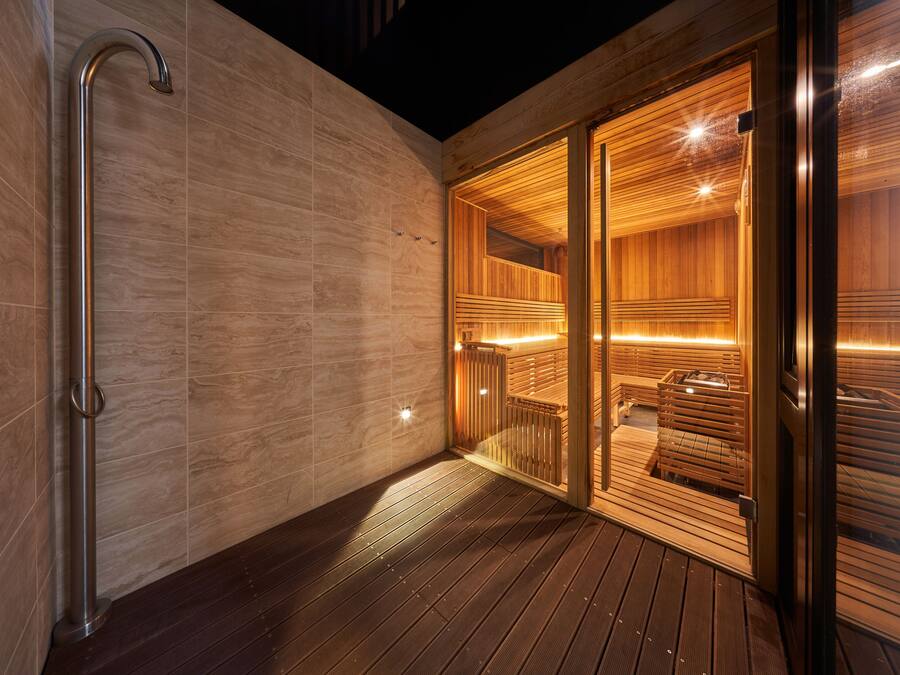 A modern sauna with wooden walls and a glass door, a metal handrail, and a wooden deck.