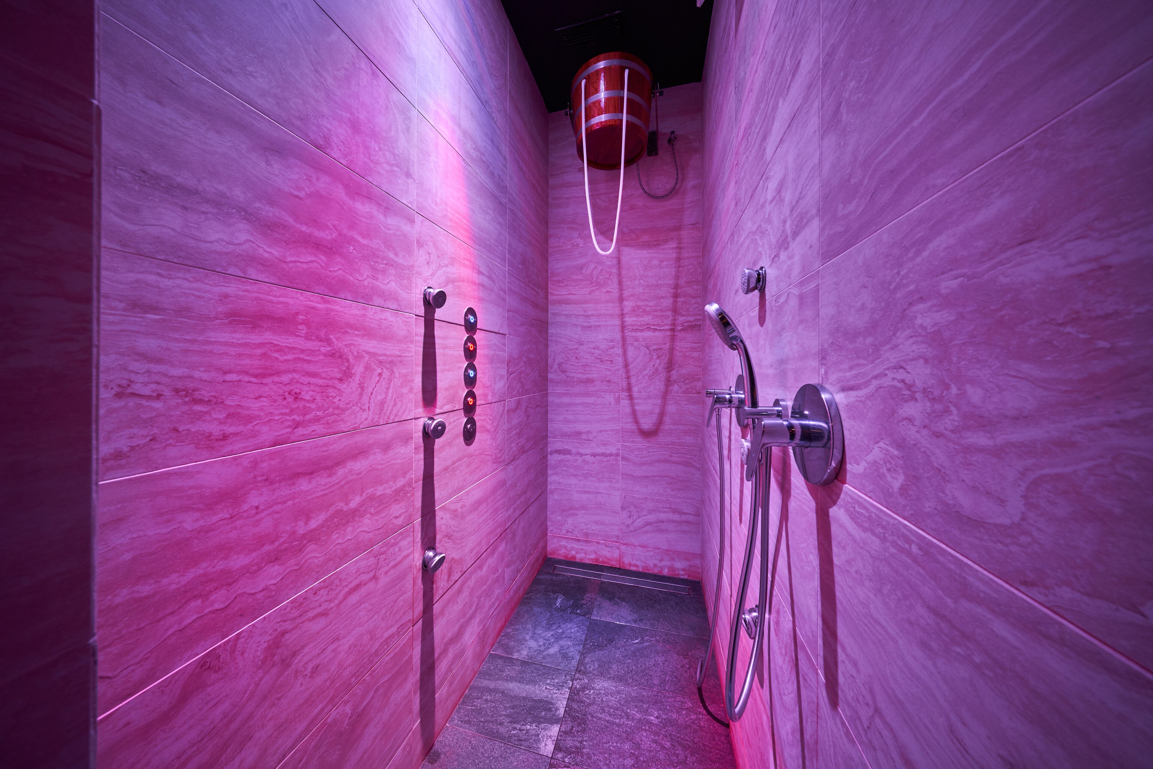 Een moderne badkamer met roze marmeren wanden, een douchegedeelte en een zichtbare boiler.