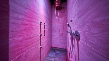 Un baño moderno con paredes de mármol rosa, zona de ducha y calentador de agua a la vista.