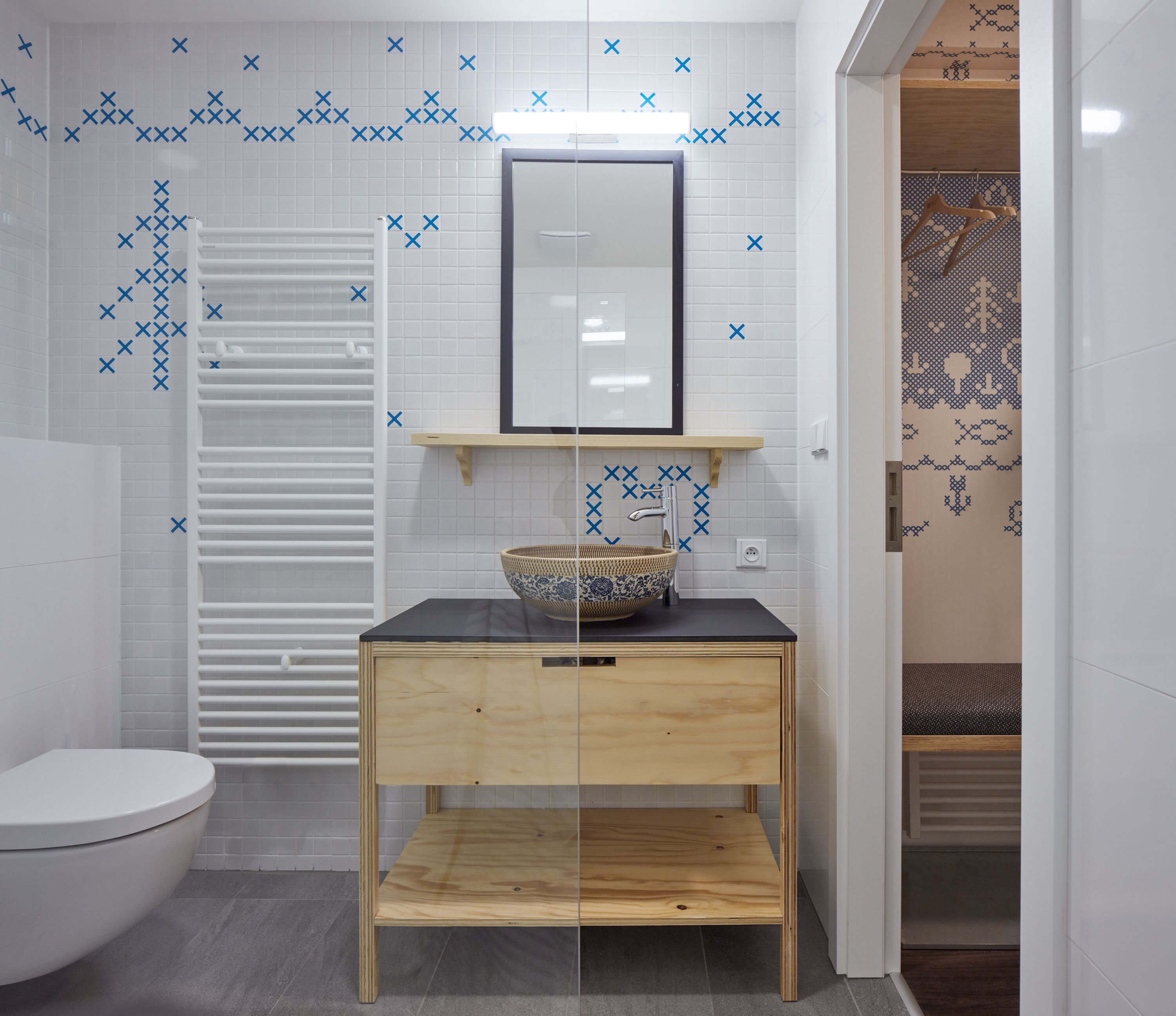 A bathroom with a toilet, a sink with a decorative bowl, and a mirror above it. There is a towel rack and a shelf with a basket.