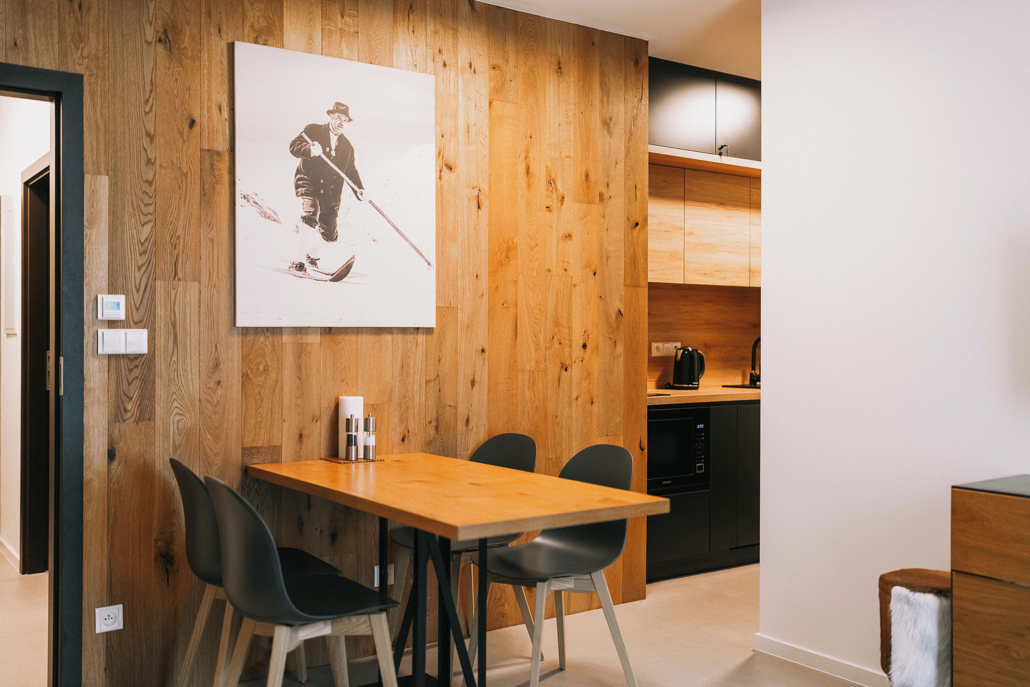 A modern kitchen with wooden cabinetry, a dining table with chairs, and a wall-mounted artwork.