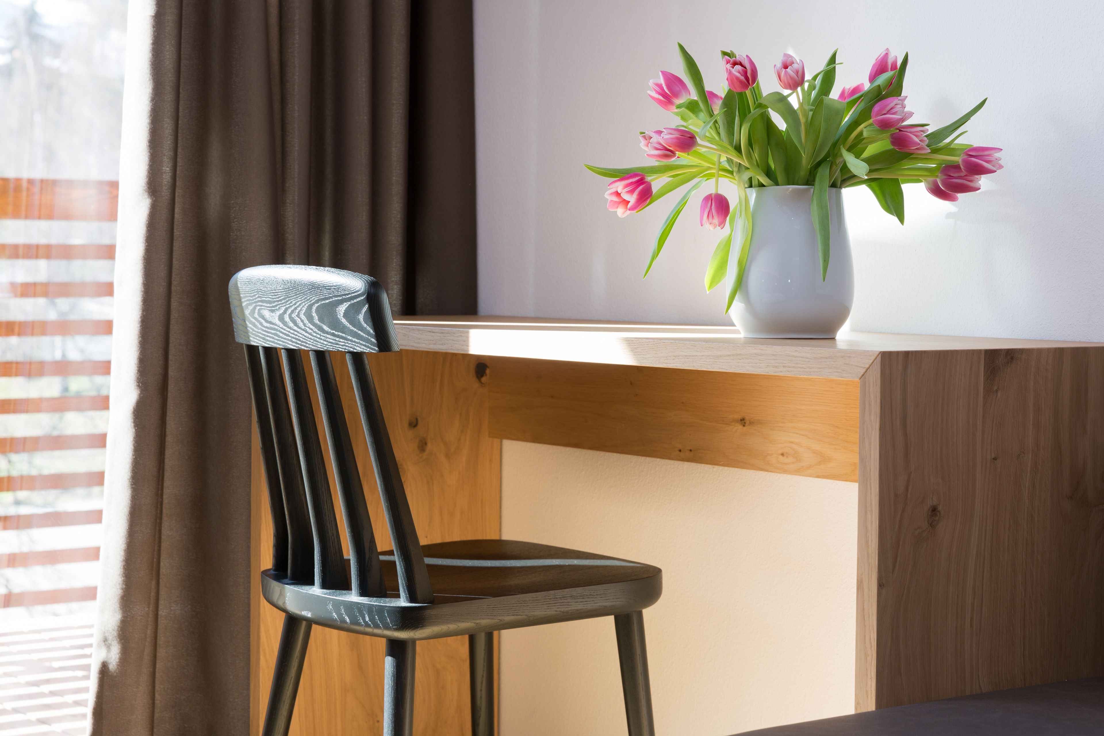 A wooden desk with a white vase containing pink tulips.