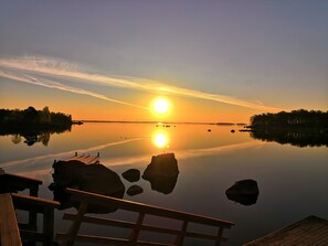 A calm lake at sunset with a wooden dock and rocks in the foreground.