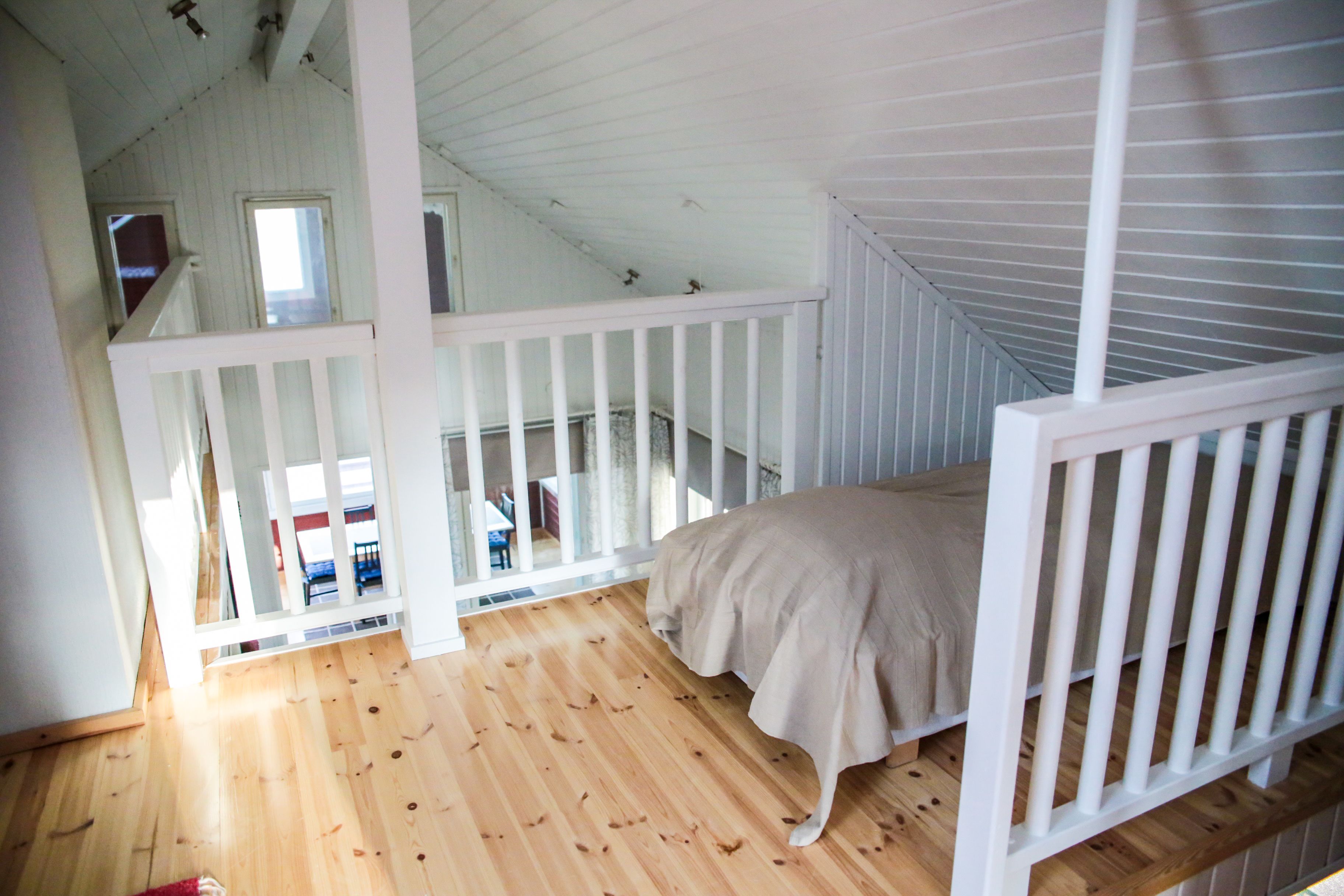 A high-ceilinged room with a wooden floor, a bunk bed, and a white railing.