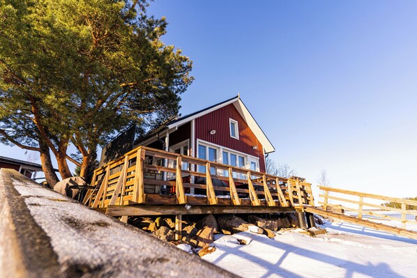 A wooden deck with a railing leading to a red building with a white window.