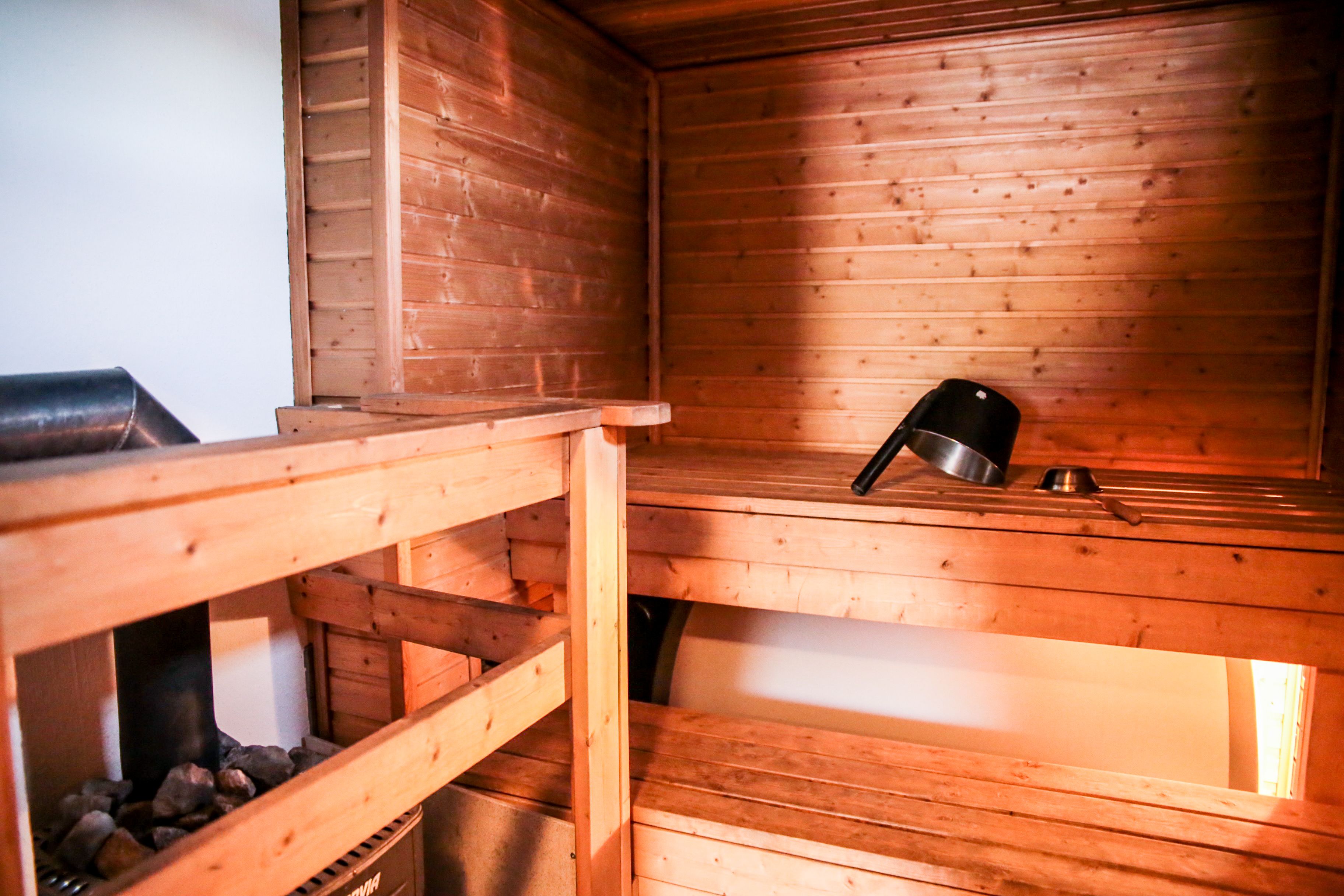 Una sauna con paredes y bancos de madera, un calentador metálico y un pequeño recipiente metálico en el banco.