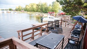 A wooden dock with a table and chairs, overlooking a calm lake with boats.