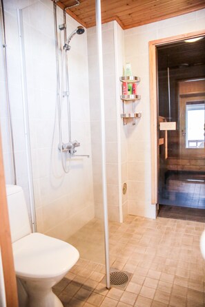A bathroom with a shower, toilet, and a shelf with toiletries.