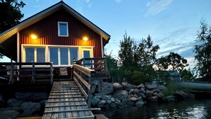 A wooden dock leading to a cabin with a small porch and a window.