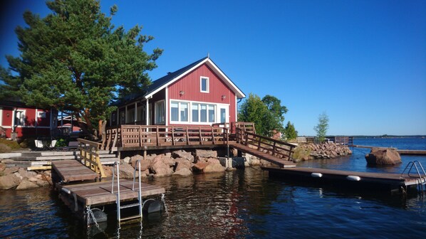 A red wooden house with a dock, surrounded by rocks and trees.