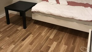 A small bedroom with a bed, a nightstand, and a wooden floor.