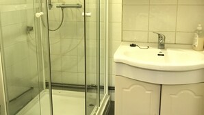 A bathroom with a glass-enclosed shower, a white sink, and wooden cabinets.
