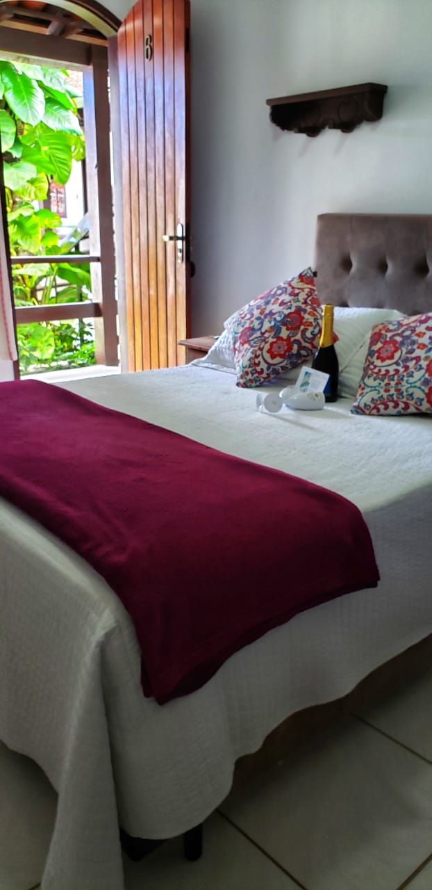 Una cama con una manta roja, almohadas estampadas y una botella de champán.