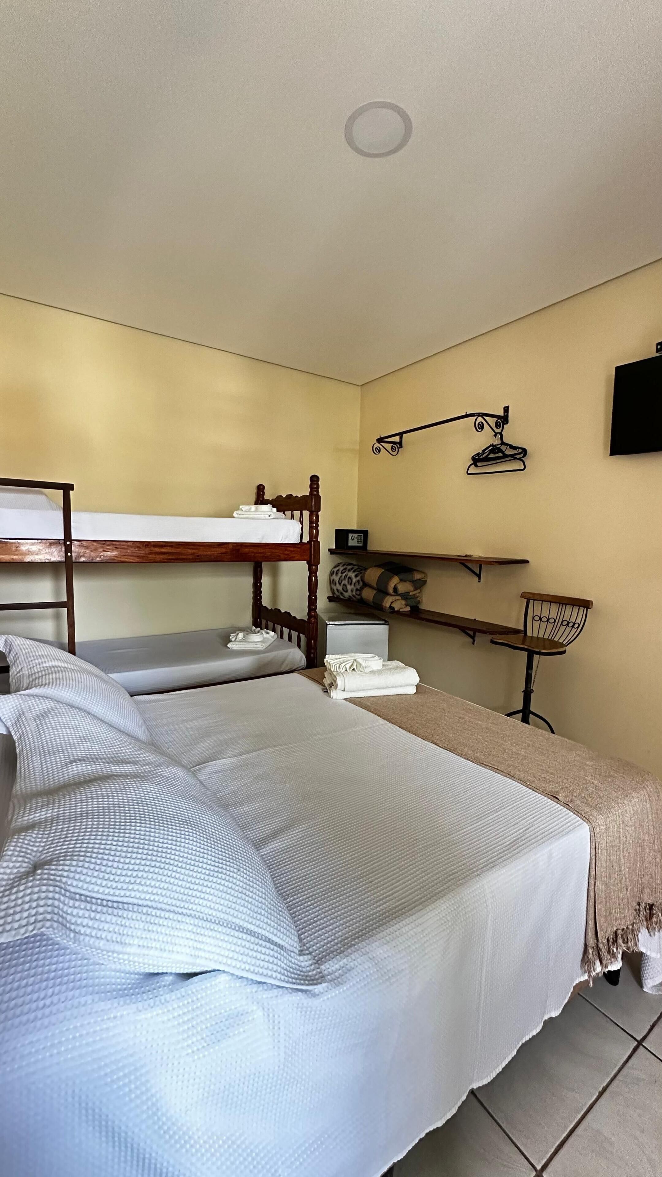 A dormitory room with bunk beds, a desk, a chair, and a shelf with personal items.