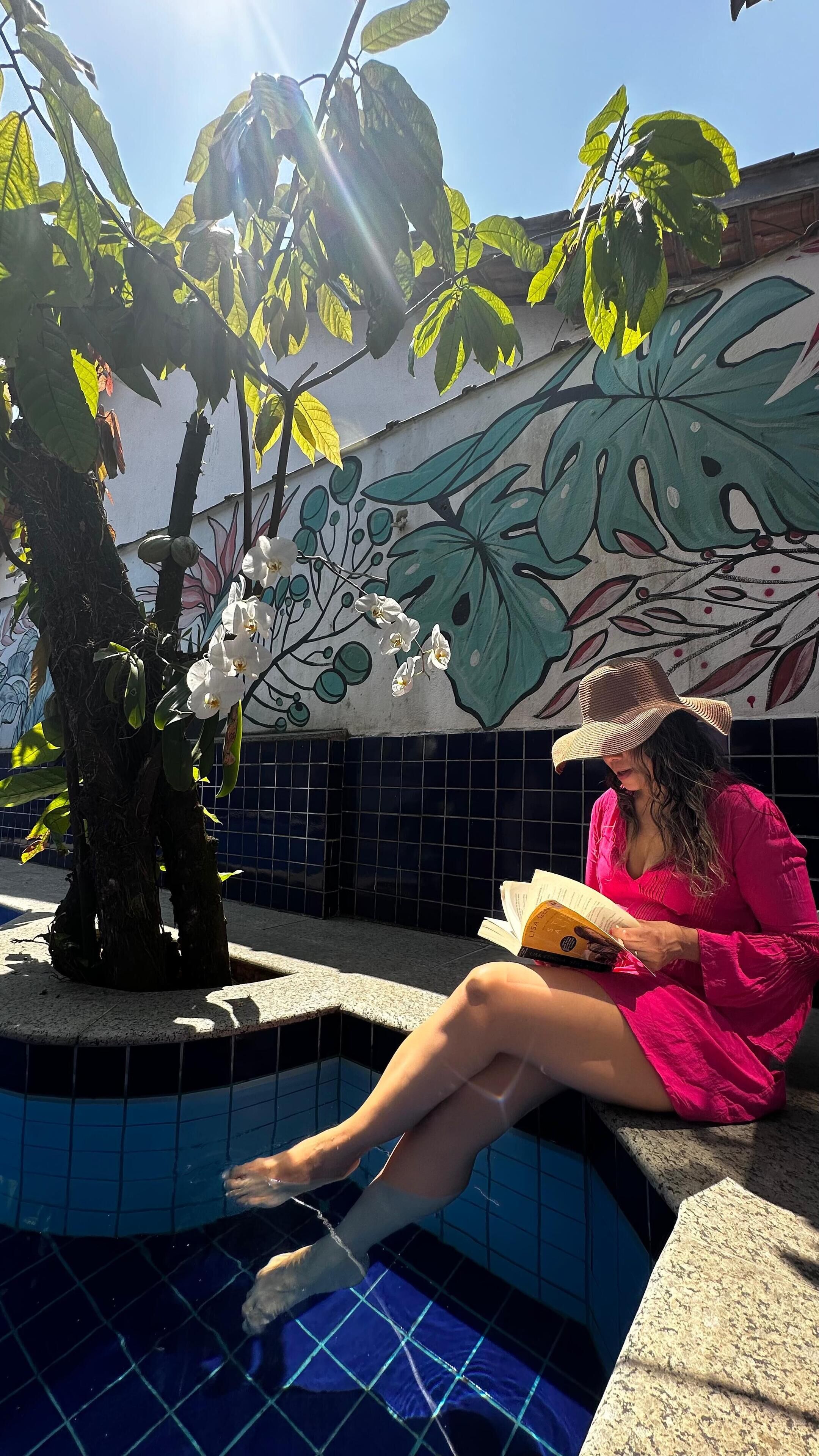 Eine Person liest am Pool ein Buch, im Hintergrund ist ein Wandgemälde zu sehen.