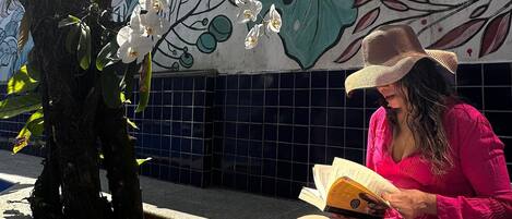 Una persona leyendo un libro junto a una piscina, con un mural al fondo.