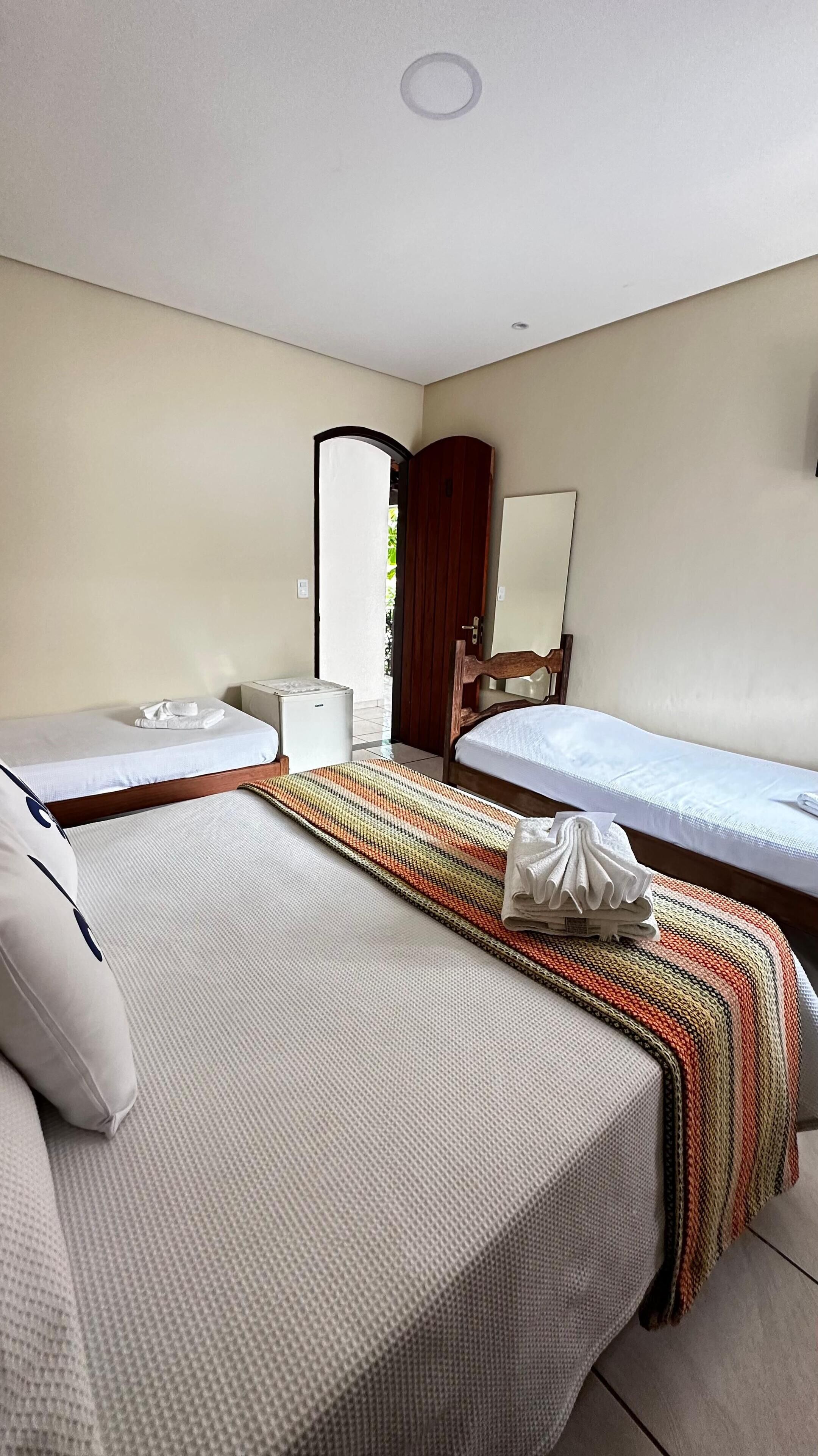 A hotel room with two single beds, a wooden wardrobe, a bedside table, a mirror, and a small white appliance.