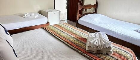 A hotel room with two single beds, a wooden wardrobe, a bedside table, a mirror, and a small white appliance.