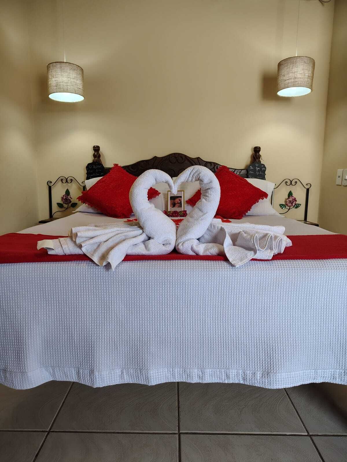 A bed with a heart-shaped towel arrangement, a red pillow, and a decorative headboard.