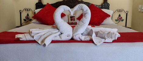 A bed with a heart-shaped towel arrangement, a red pillow, and a decorative headboard.
