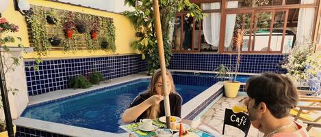 Ett område vid poolen med en pool som har kakelbeklädd botten, ett bord med en kopp och mat, och en skylt med texten "Café".