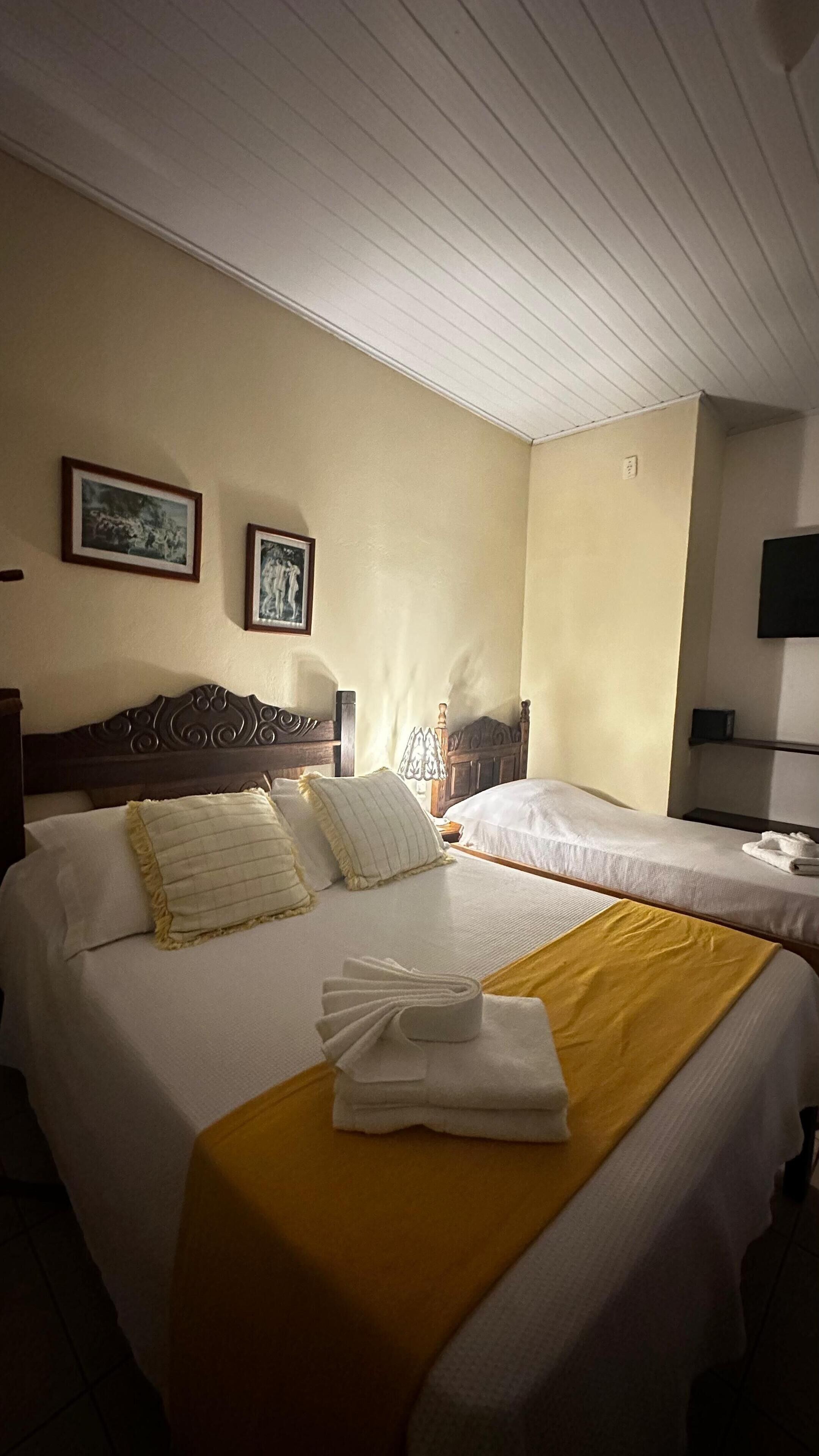 Habitación de hotel con dos camas, cabecero de madera, manta amarilla y televisión de pantalla plana en la pared.
