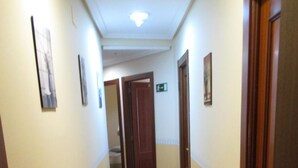 A narrow hallway with wooden flooring and cream-colored walls, leading to a door at the end. - Hostal Becares (Palencia)