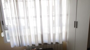 A room with a wooden floor, a table with a fruit bowl, a bed with a patterned blanket, and a wardrobe. - Hostal Becares (Palencia)