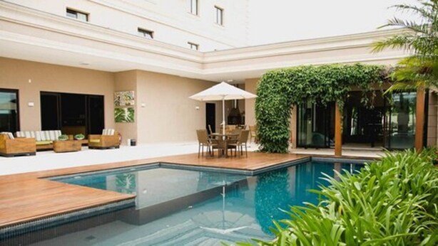 A modern indoor swimming pool with a wooden deck, surrounded by a lounge area with seating and a covered table. - Class Hotel Alfenas (Alfenas)