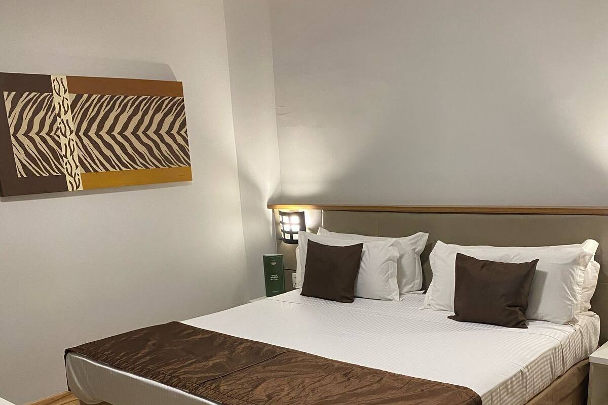 Une chambre d’hôtel bien aménagée, avec un grand lit, une table de chevet, une chaise et une lampe fixée au mur.