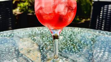 A glass of red drink with a lemon slice on a glass table outdoors.