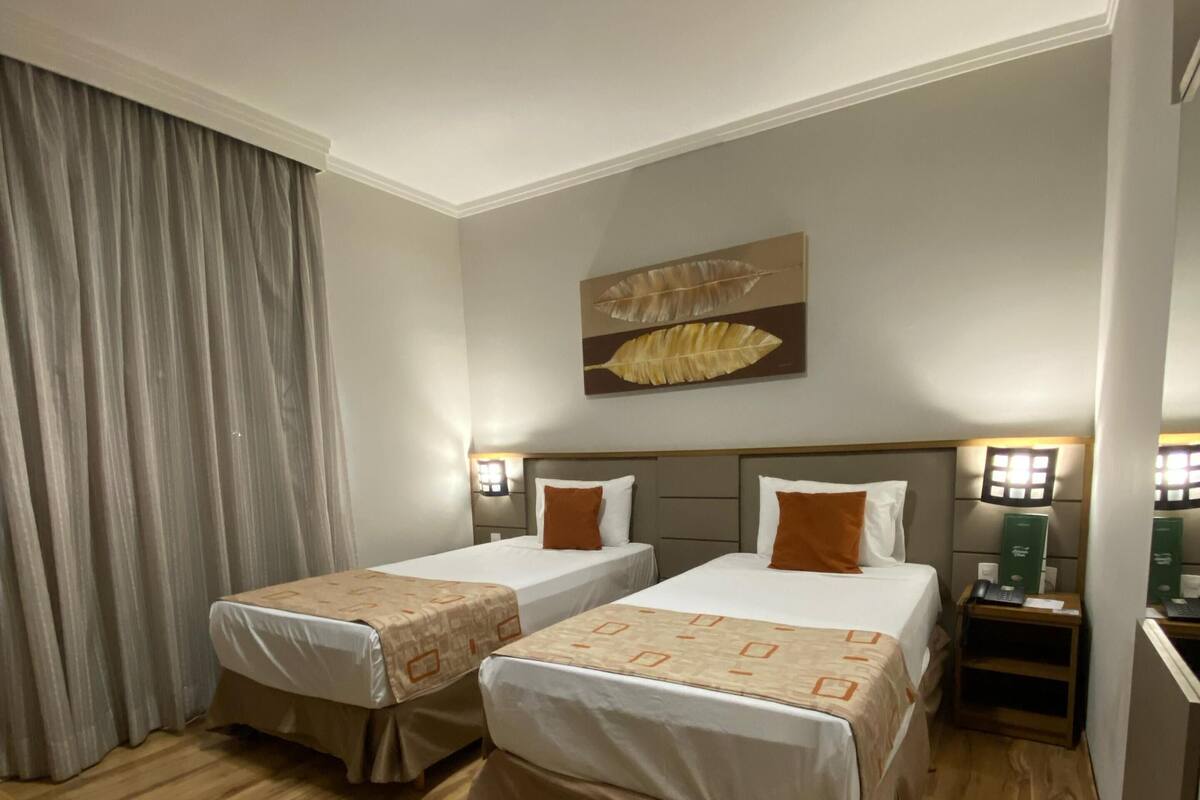 Une chambre d’hôtel avec deux lits, un plancher en bois, une grande fenêtre avec des rideaux et un tableau au mur.