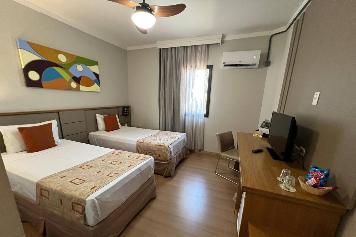Une chambre d’hôtel avec deux lits, un bureau avec un ordinateur, une chaise et un appareil de climatisation.