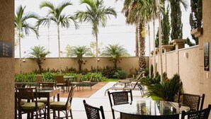 An outdoor dining area with tables and chairs, surrounded by palm trees and greenery. - Class Hotel Alfenas (Alfenas)