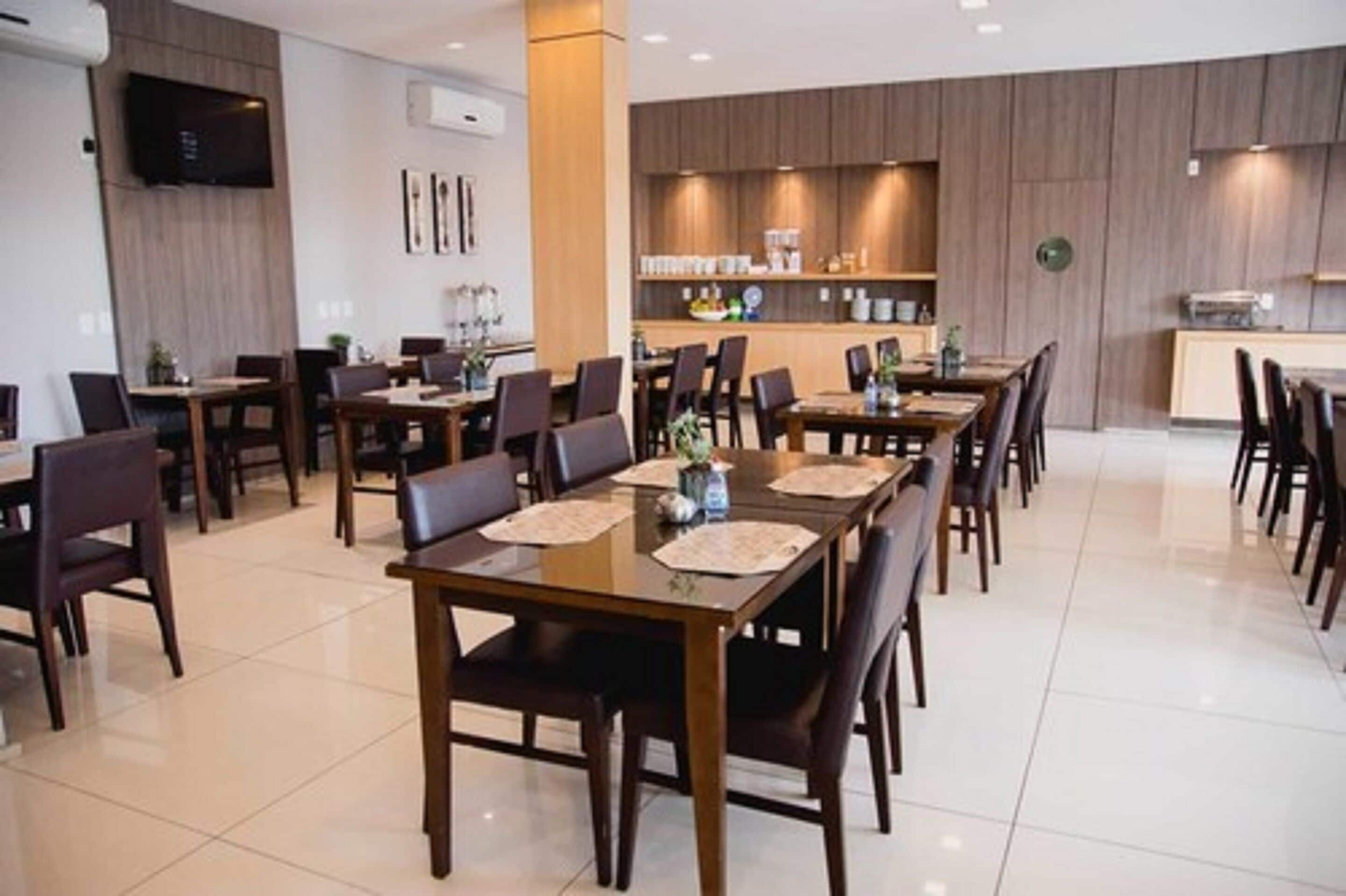 Un espace repas moderne avec plusieurs tables et chaises, une cuisine à l’arrière-plan et un téléviseur à écran plat fixé au mur.