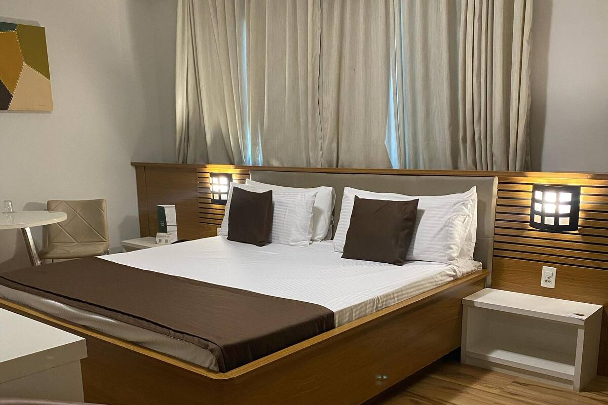Une chambre d’hôtel moderne avec un lit en bois, une table de chevet, une chaise et un bureau.