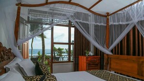 Ein Schlafzimmer mit einem großen Bett, einem Holzkopfstück und Meerblick durch ein großes Fenster.