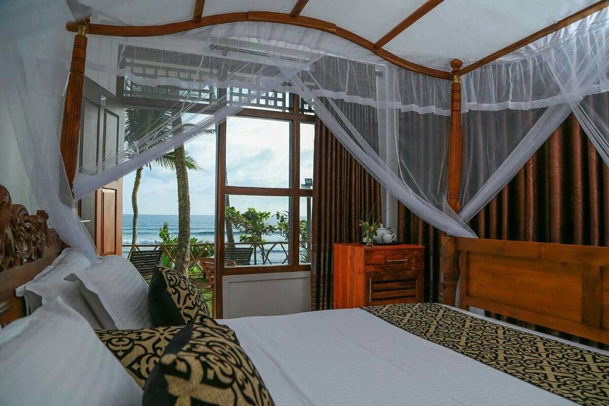 A bedroom with a large bed, a wooden headboard, and a view of the ocean through a large window.