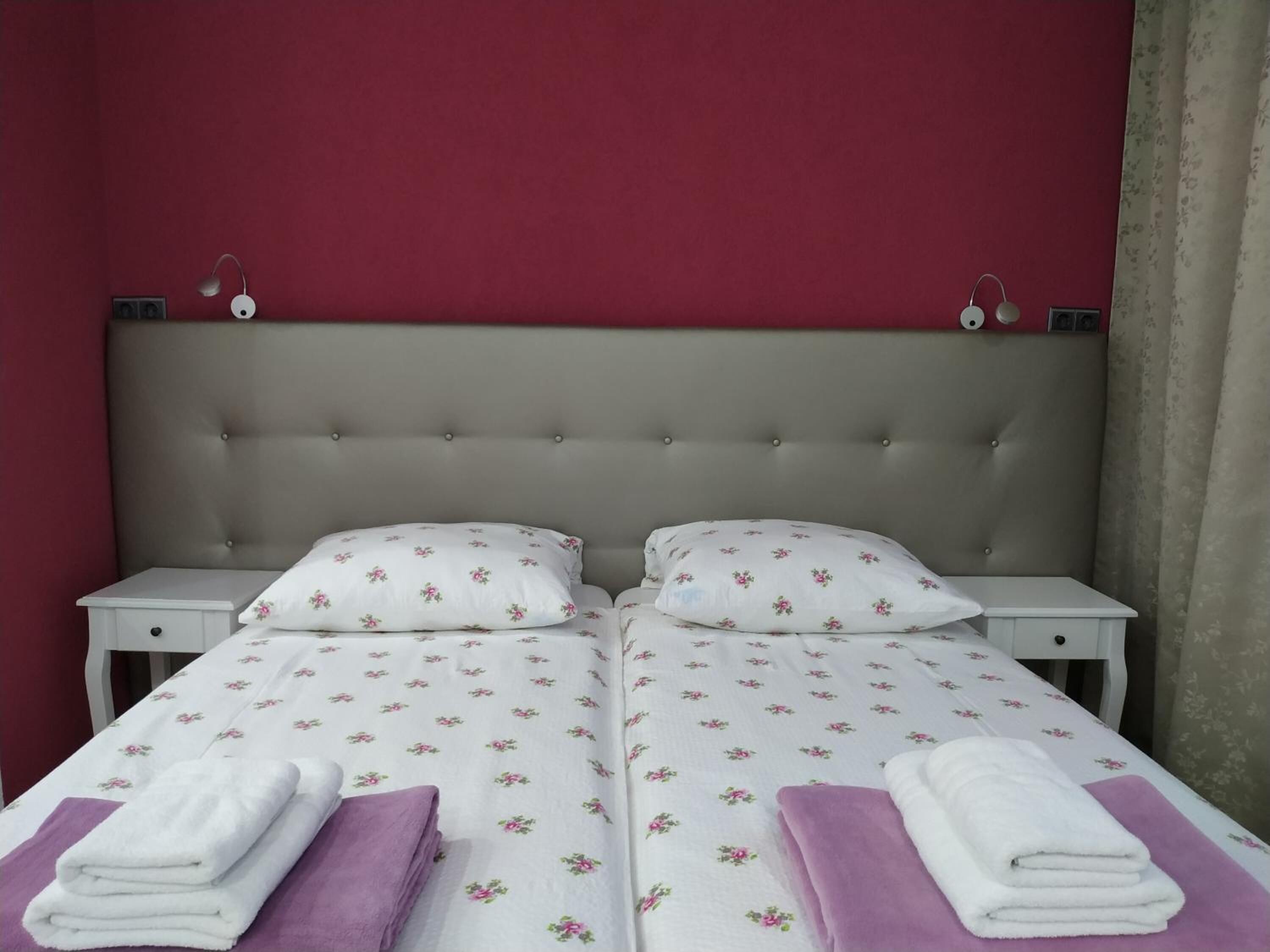 Habitación doble con dos camas, cada una con colcha y almohadas de estampado floral. Hay dos mesitas de noche con lámparas, y la habitación tiene una pared de acento roja.