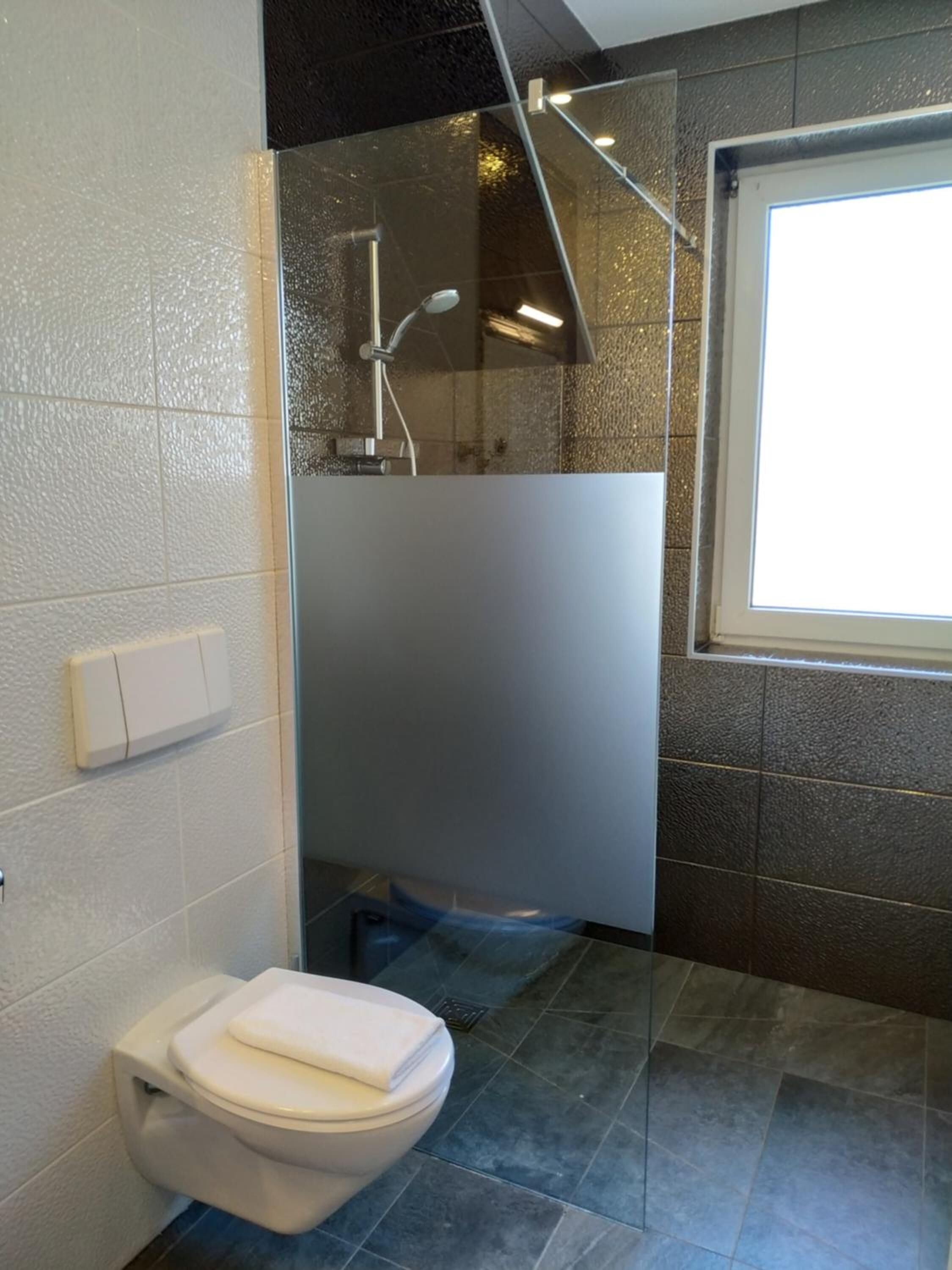 Een moderne badkamer met toilet, een douchecabine van glas en een raam.