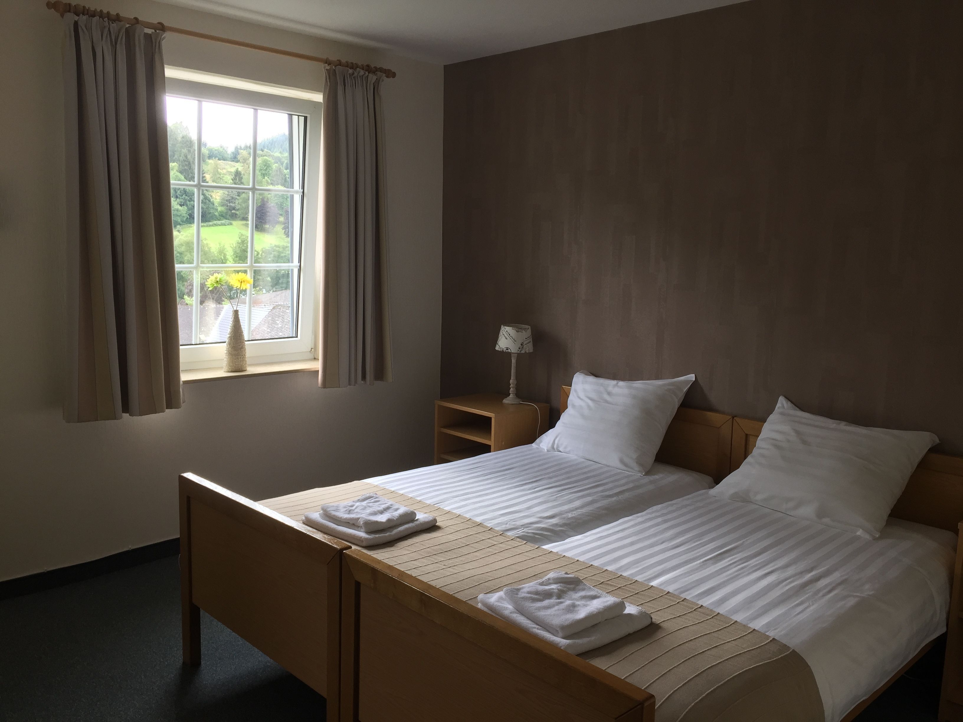 Ein Hotelzimmer mit einem Bett, einem Nachttisch, einer Lampe und einem Fenster mit Vorhängen.