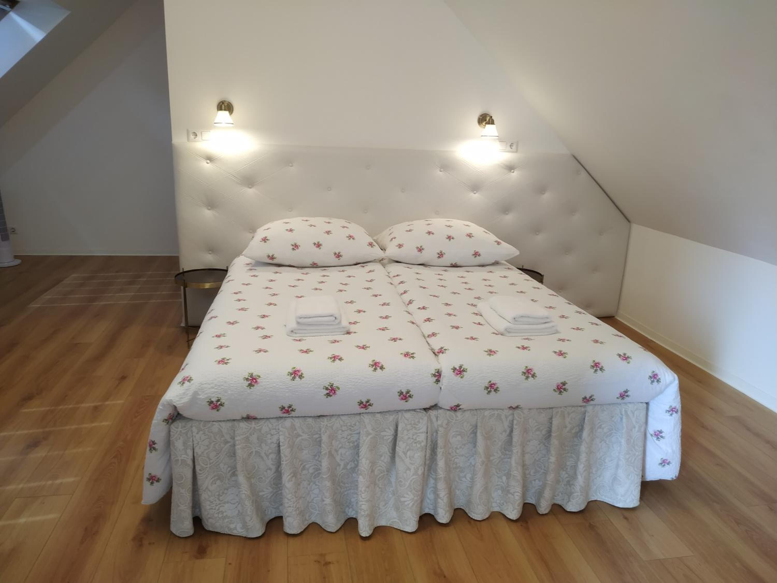 Un dormitorio con cabecera capitonada, dos almohadas, una cama con colcha floral y dos lámparas de pared.